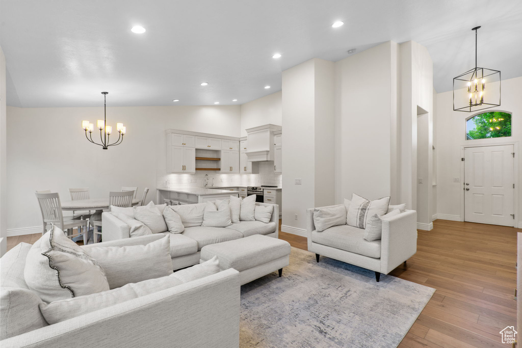Living room featuring a towering ceiling, baseboards, an inviting chandelier, recessed lighting, and light wood-style flooring