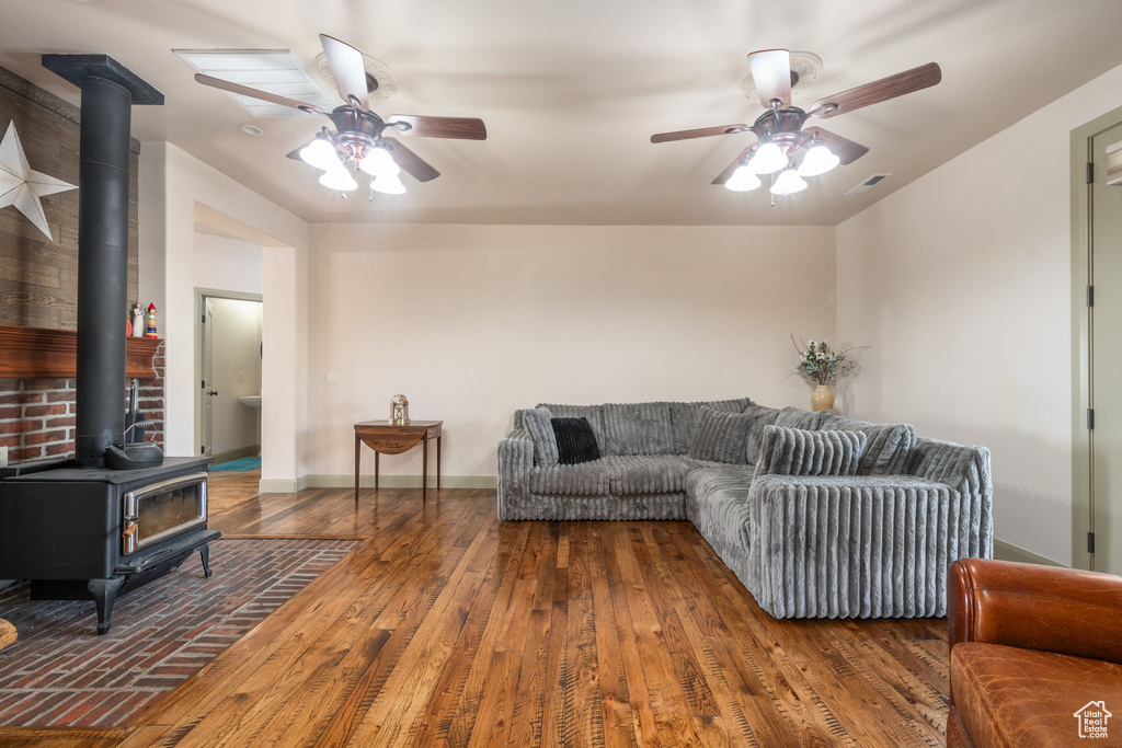 Living area with ceiling fan, a wood stove, wood finished floors, and visible vents