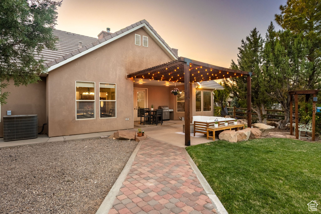 Back of property at dusk featuring central AC, stucco siding, outdoor lounge area, a lawn, and a patio