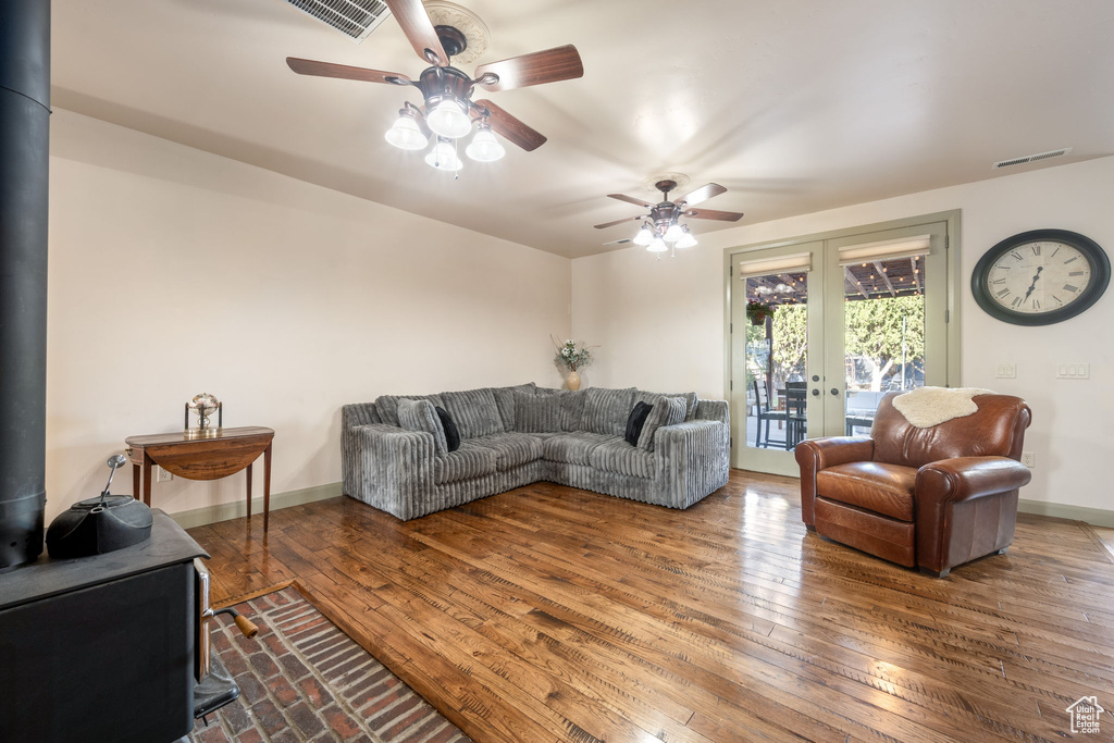 Living area with a wood stove, french doors, a ceiling fan, visible vents, and hardwood / wood-style flooring