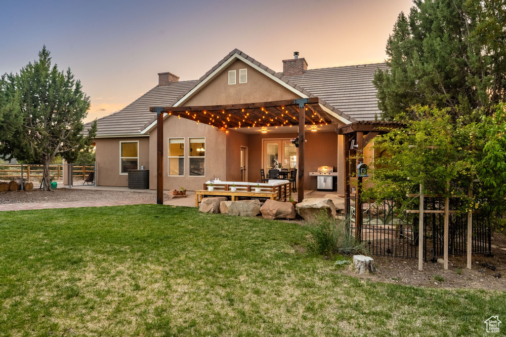 Back of house at dusk with a chimney, a lawn, fence, a patio, and stucco siding