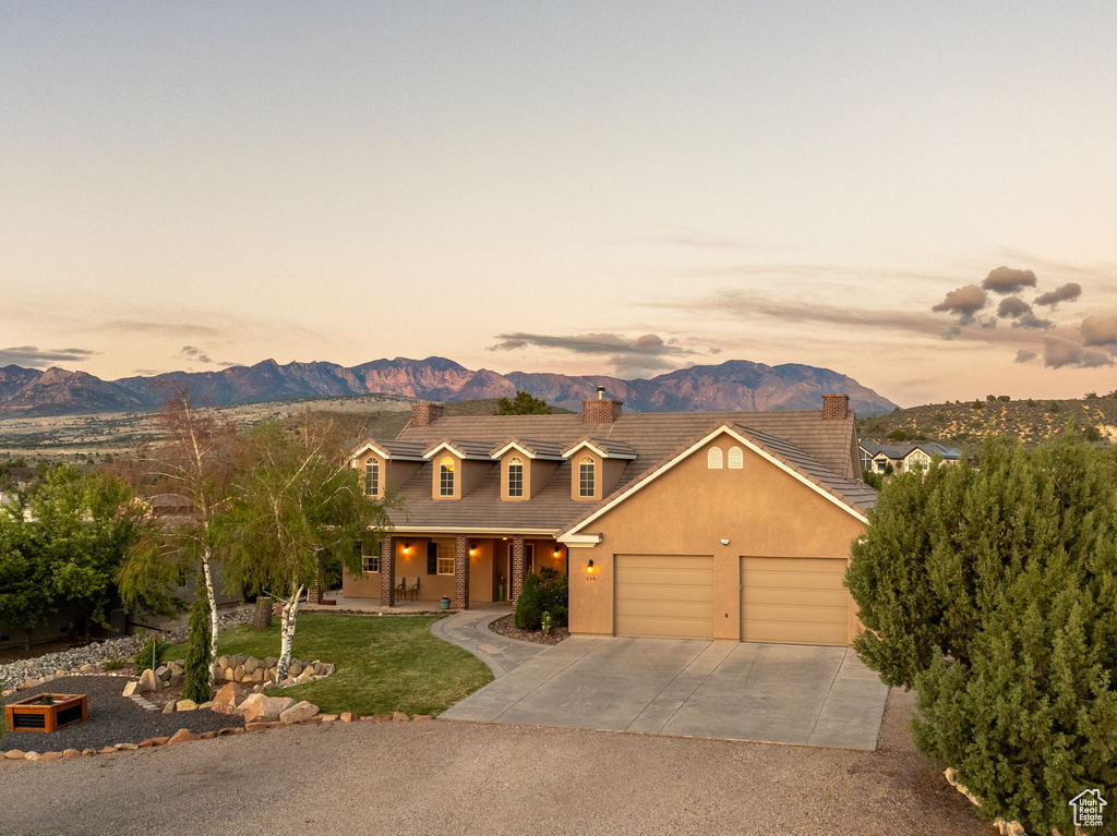 View of front facade featuring an attached garage, a mountain view, a chimney, concrete driveway, and covered porch