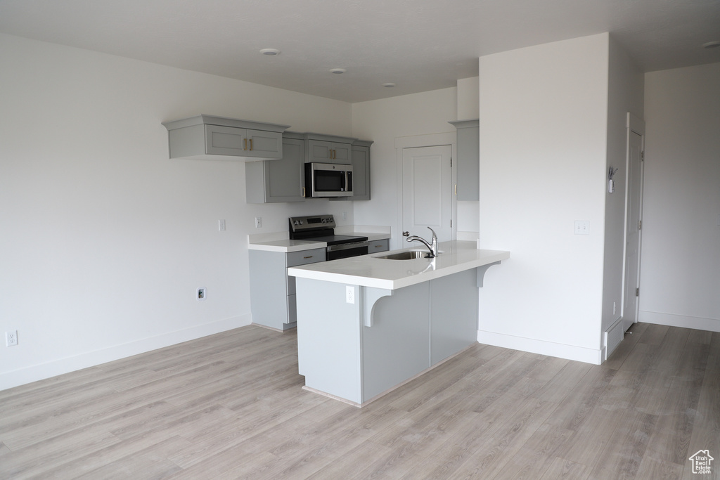 Kitchen with light wood-style floors, a kitchen bar, a sink, gray cabinetry, and stainless steel appliances