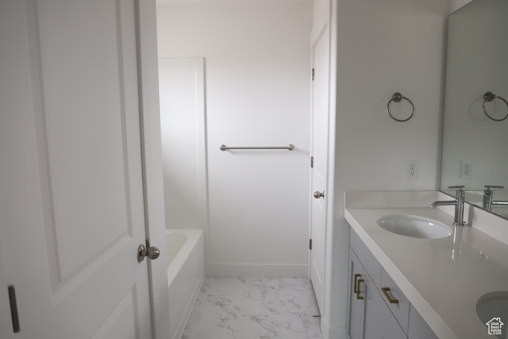Full bath featuring a sink, double vanity, marble finish floor, baseboards, and a bath