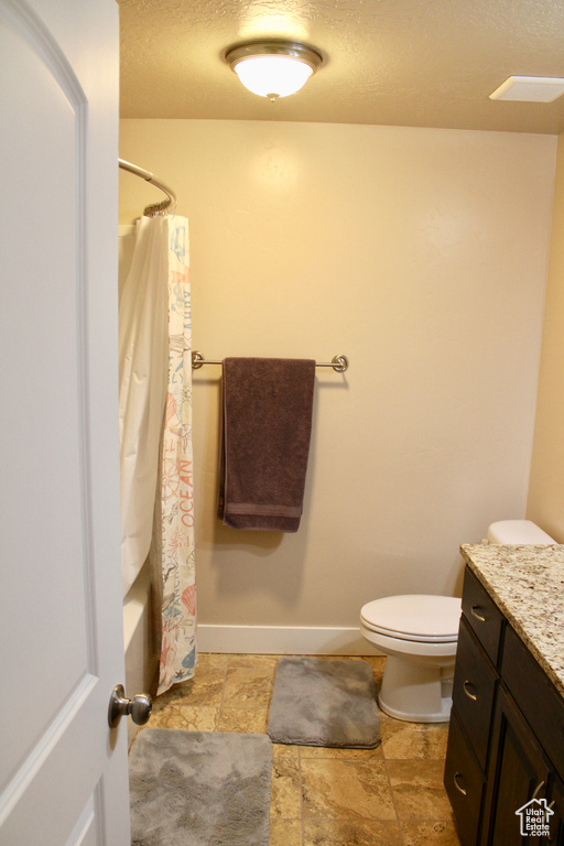 Full bathroom with vanity, a textured ceiling, stone finish floor, and toilet