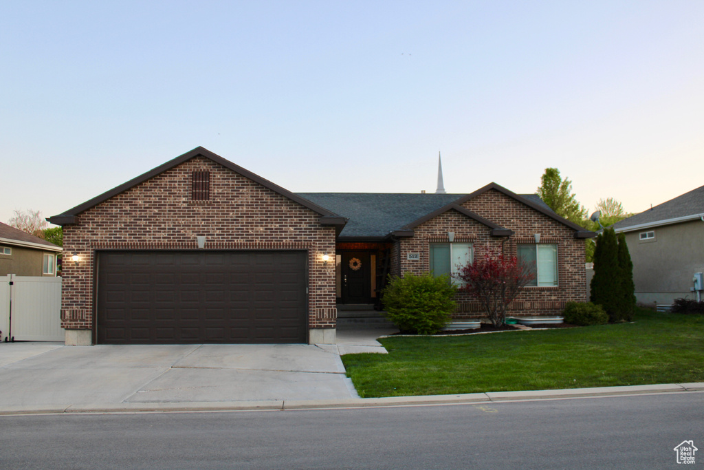 Ranch-style house with a yard, brick siding, fence, concrete driveway, and an attached garage