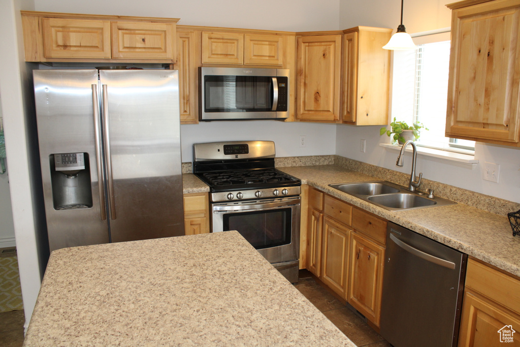 Kitchen featuring light brown cabinetry, hanging light fixtures, a sink, light countertops, and stainless steel appliances