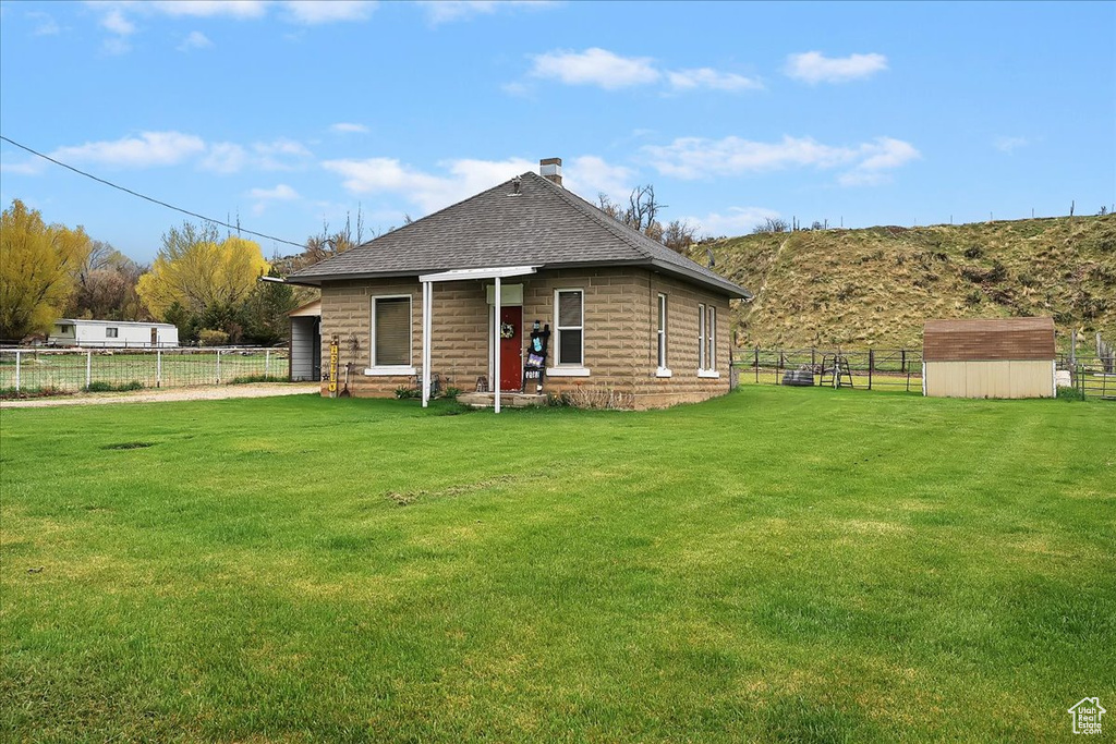 Back of property with a lawn, a fenced backyard, roof with shingles, and a storage unit