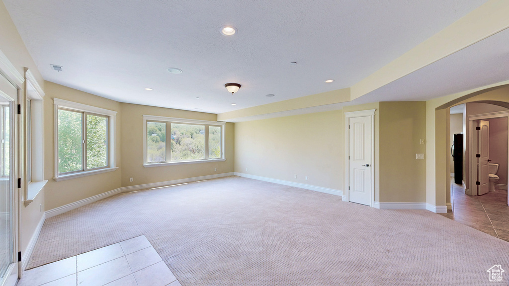 Unfurnished room featuring light tile patterned floors, arched walkways, baseboards, and light colored carpet
