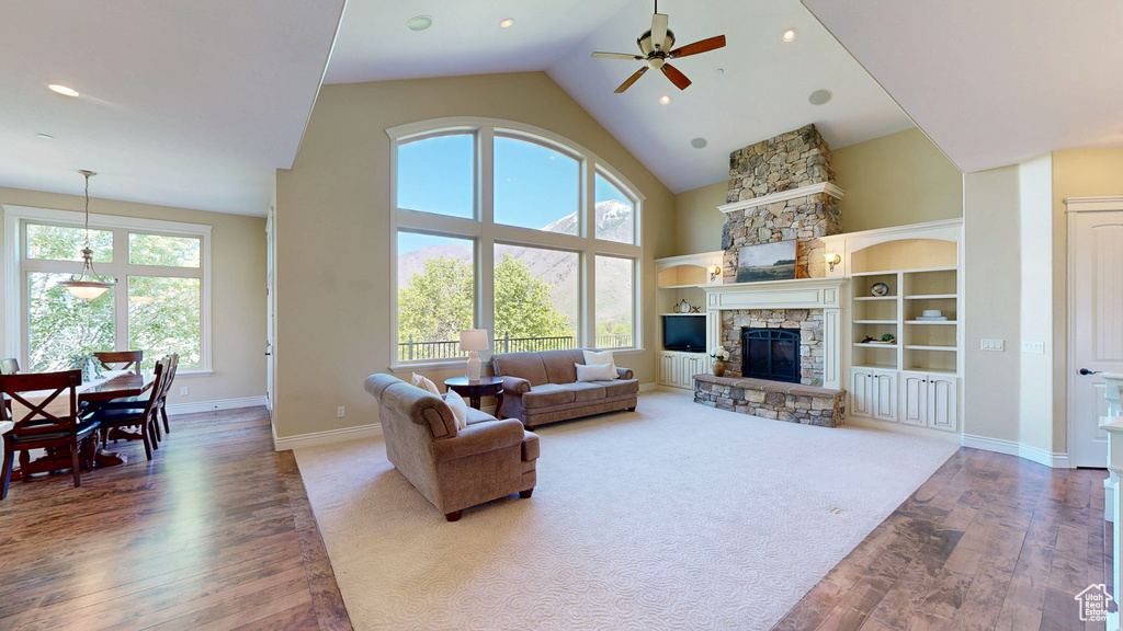Living room with ceiling fan, a stone fireplace, wood finished floors, high vaulted ceiling, and baseboards