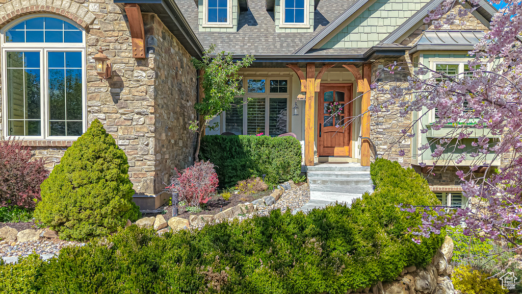View of exterior entry featuring a shingled roof and stone siding