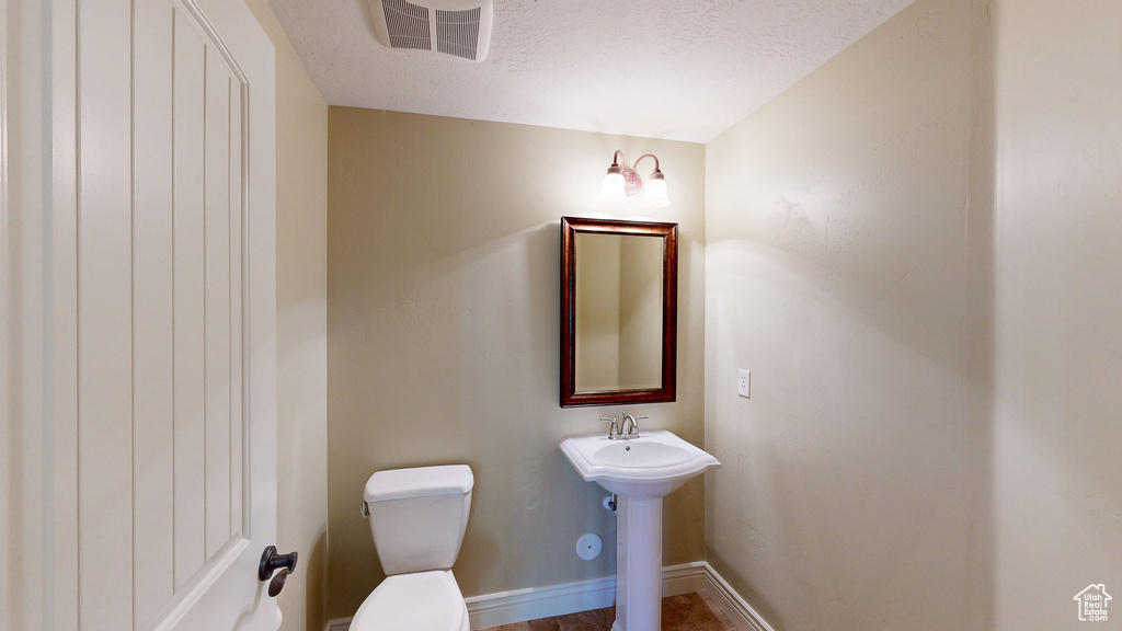 Half bath featuring a sink, toilet, a textured ceiling, baseboards, and visible vents