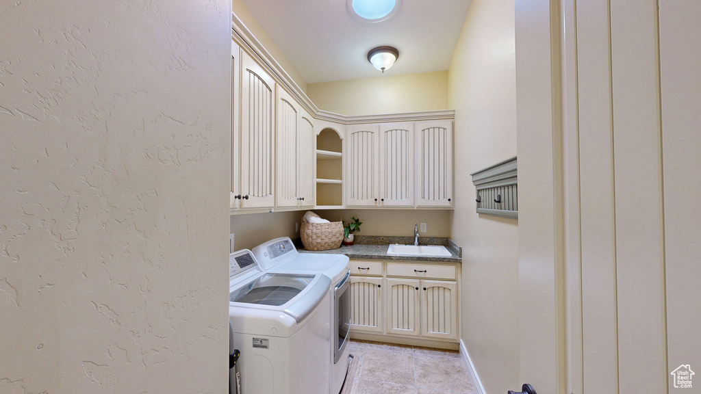 Washroom with a textured wall, a sink, cabinet space, independent washer and dryer, and light tile patterned floors