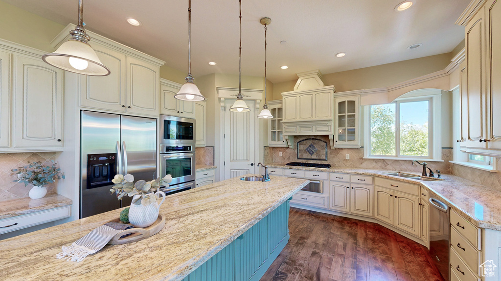 Kitchen with a sink, appliances with stainless steel finishes, glass insert cabinets, and dark wood-type flooring