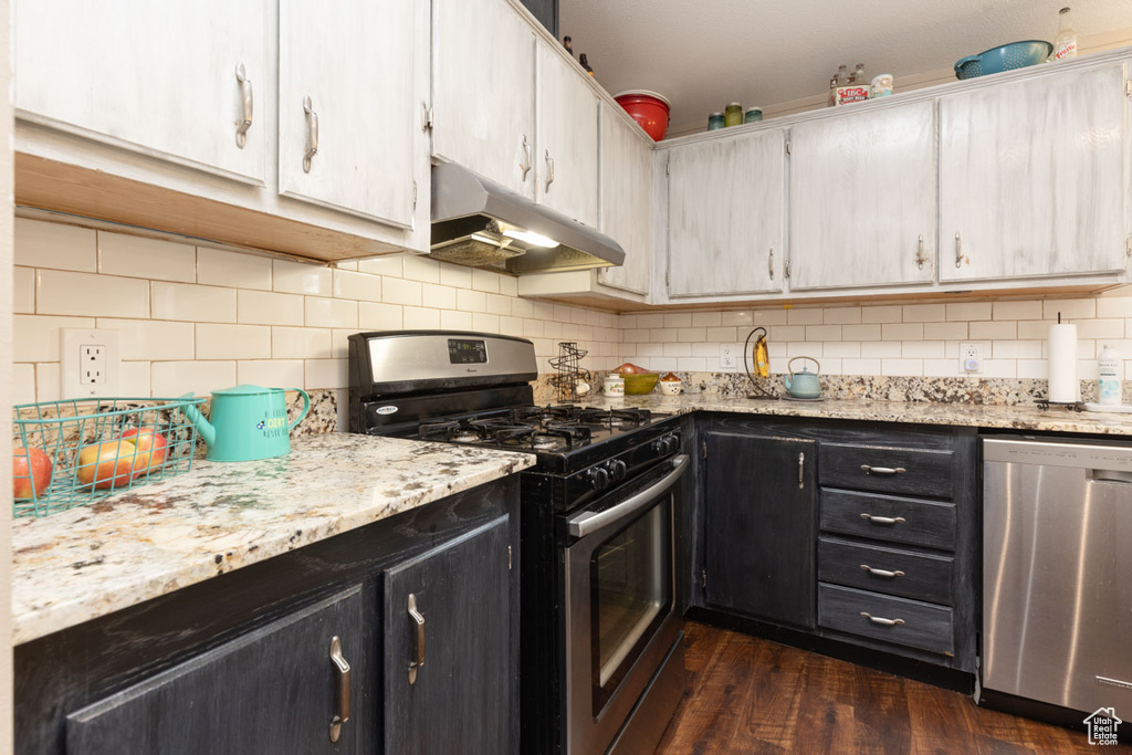 Kitchen with decorative backsplash, under cabinet range hood, dark wood-style floors, and stainless steel appliances