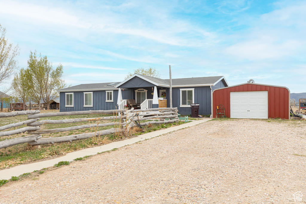Ranch-style house with a fenced front yard, dirt driveway, board and batten siding, a porch, and an outbuilding