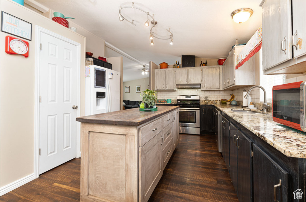 Kitchen with a kitchen island, white refrigerator with ice dispenser, gas stove, a sink, and under cabinet range hood