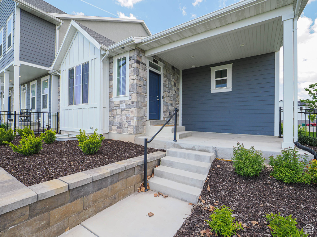 View of front facade featuring board and batten siding, fence, covered porch, and stone siding