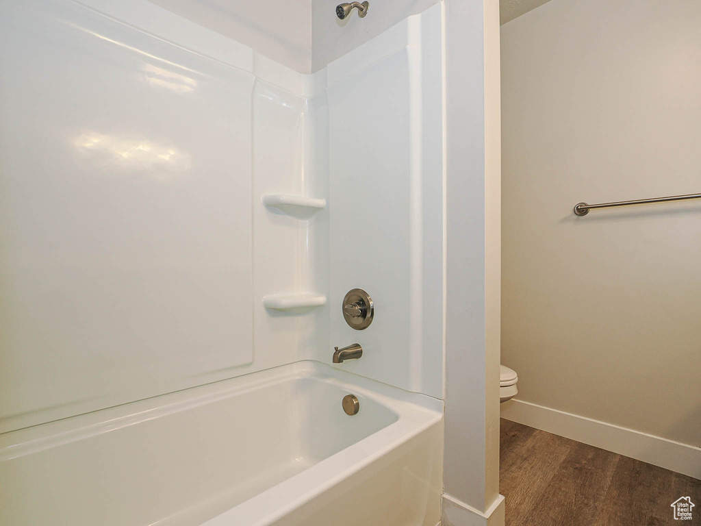 Full bath with toilet, baseboards, wood finished floors, and bathtub / shower combination