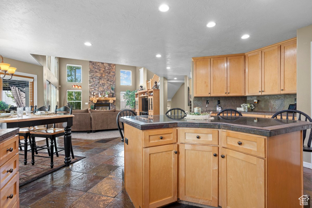 Kitchen with stone tile flooring, light brown cabinetry, dark countertops, a fireplace, and backsplash