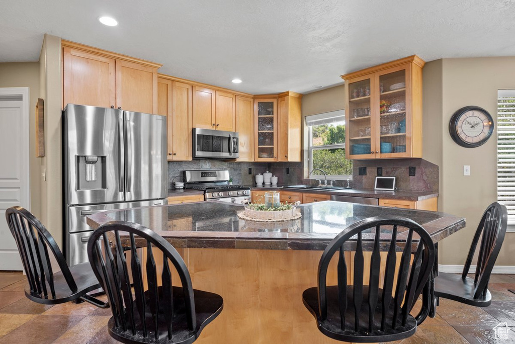 Kitchen with a breakfast bar area, appliances with stainless steel finishes, tasteful backsplash, dark countertops, and a sink