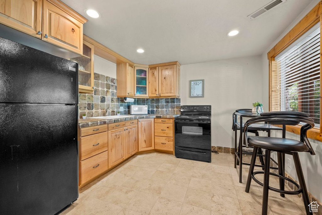 Kitchen with tile countertops, tasteful backsplash, visible vents, glass insert cabinets, and black appliances