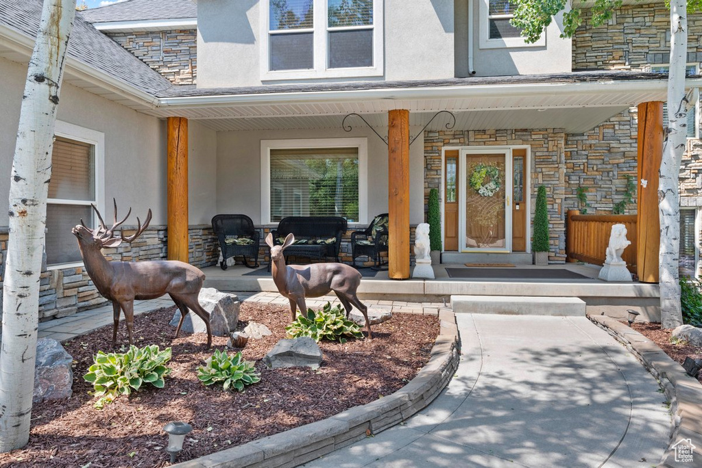 Property entrance with covered porch, stucco siding, and stone siding