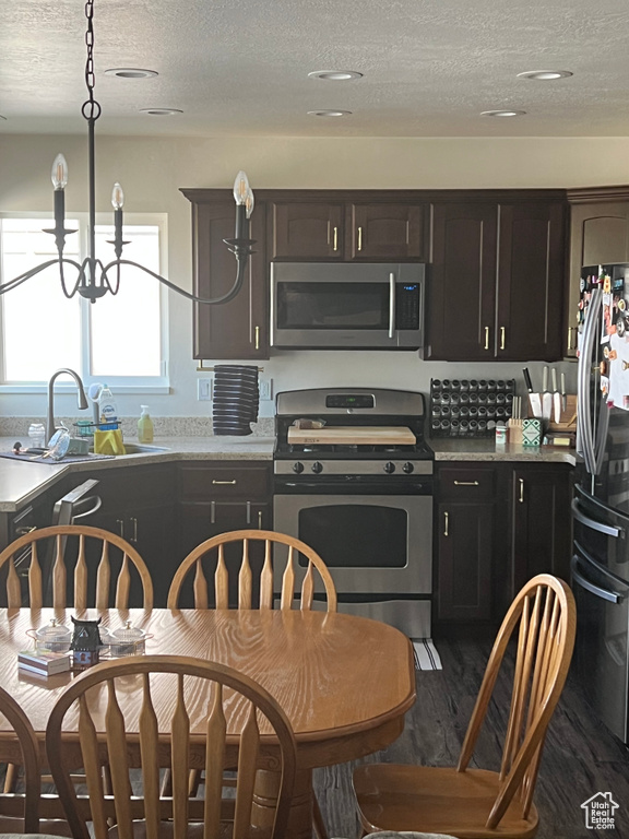 Kitchen featuring dark wood-style flooring, a textured ceiling, a sink, a chandelier, and stainless steel appliances