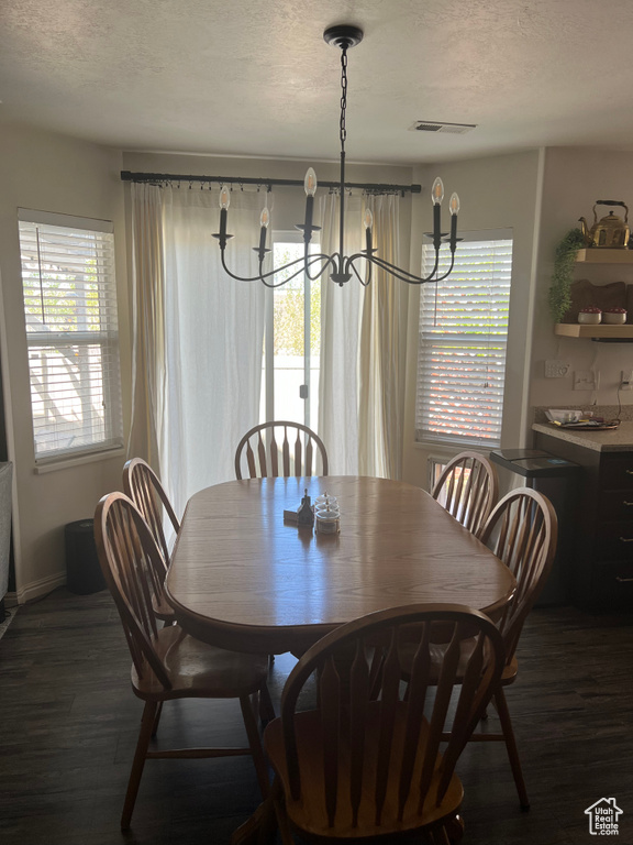 Dining area with a chandelier, a textured ceiling, visible vents, and dark wood-type flooring