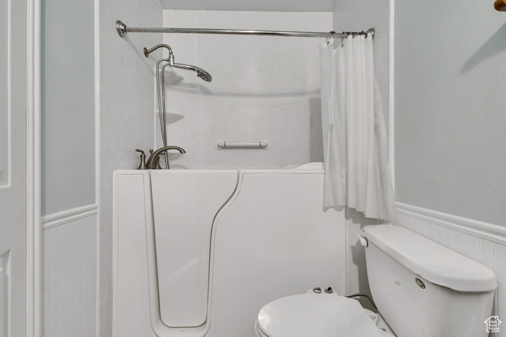 Full bath featuring a wainscoted wall, toilet, and a shower with shower curtain