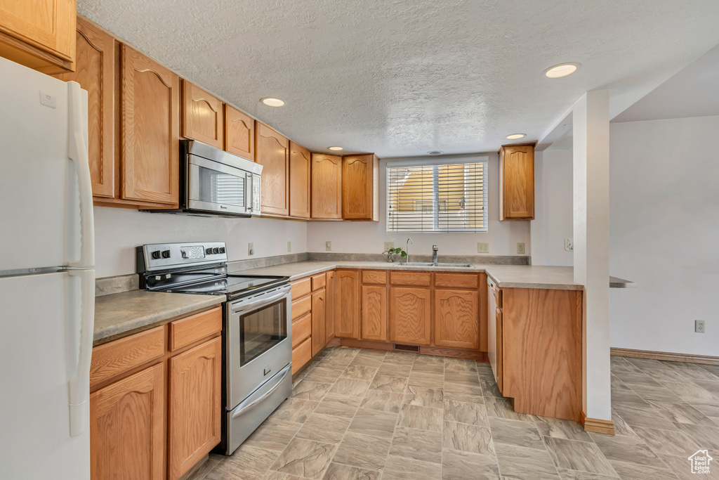 Kitchen featuring recessed lighting, light countertops, a textured ceiling, a sink, and appliances with stainless steel finishes