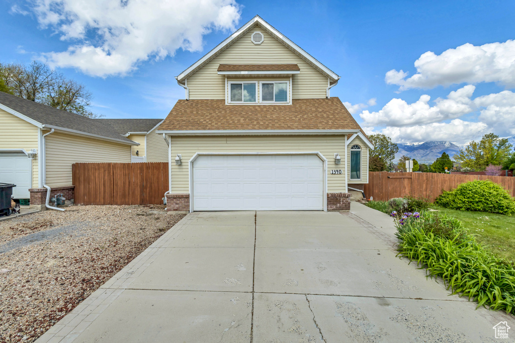 Traditional-style home featuring a garage, fence, roof with shingles, brick siding, and concrete driveway