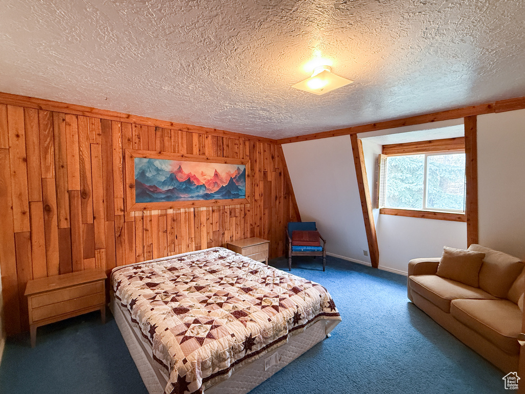 Bedroom with a textured ceiling, carpet flooring, wood walls, and baseboards