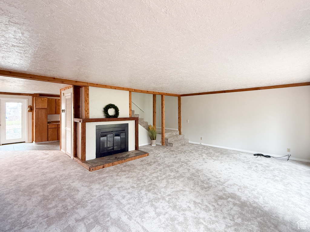 Unfurnished living room featuring carpet flooring, baseboards, a glass covered fireplace, and a textured ceiling