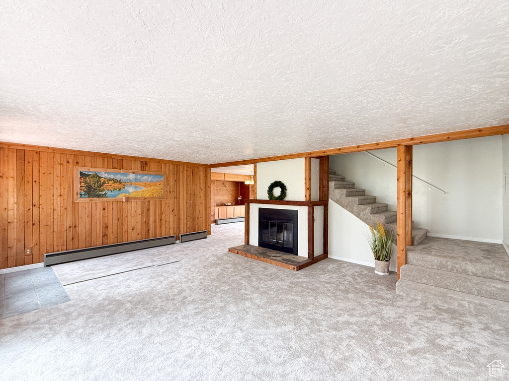 Unfurnished living room with a textured ceiling, a glass covered fireplace, stairway, wooden walls, and a baseboard radiator