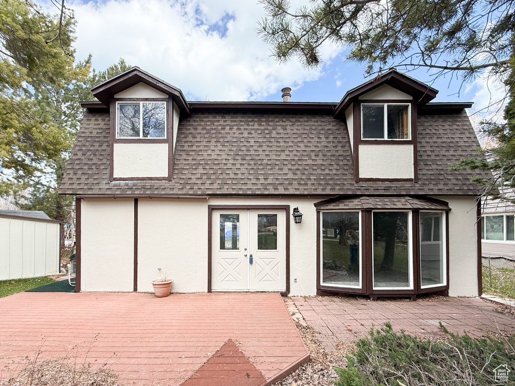 Rear view of house featuring roof with shingles, mansard roof, stucco siding, and a deck