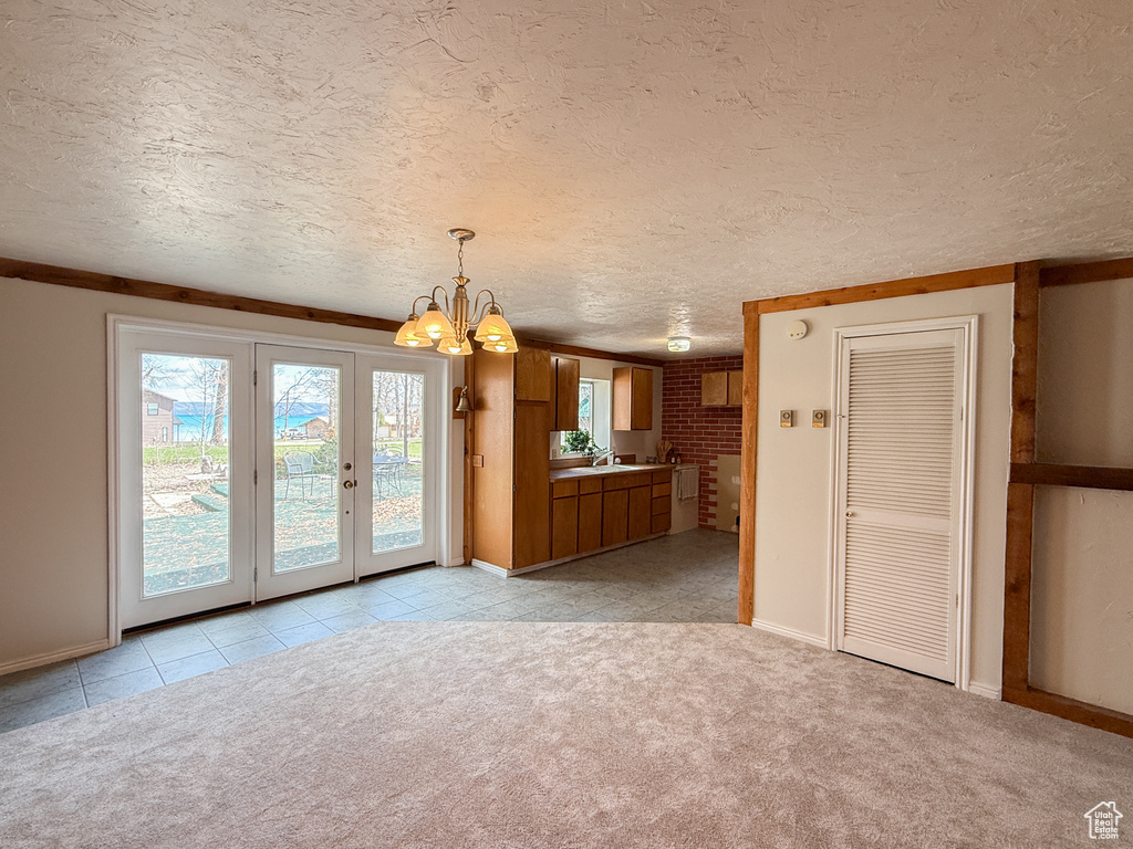 Unfurnished dining area with light carpet, a textured ceiling, a sink, baseboards, and a chandelier
