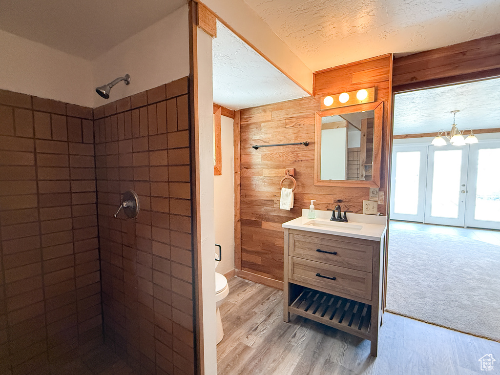 Full bath featuring toilet, wooden walls, vanity, and tiled shower