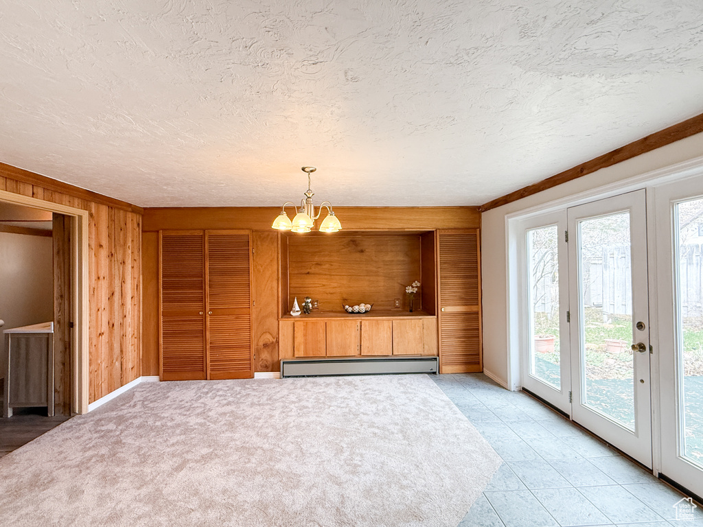 Interior space with a baseboard radiator, wood walls, a chandelier, and a textured ceiling