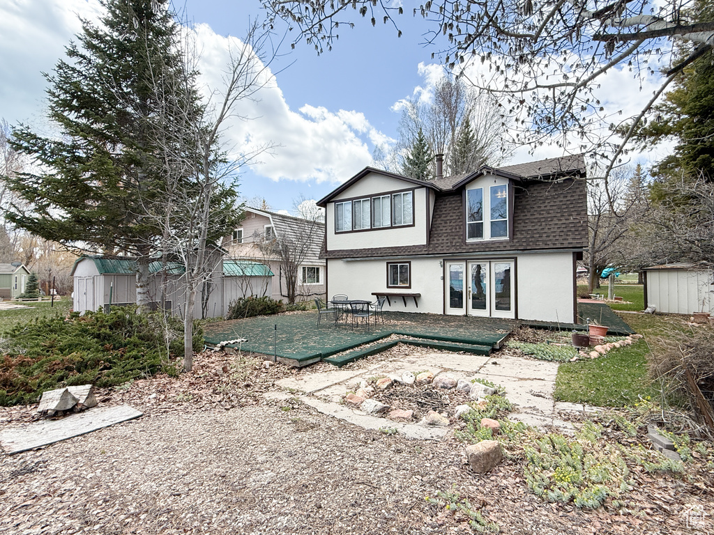 Rear view of house featuring a patio area, a storage shed, a shingled roof, an outbuilding, and stucco siding