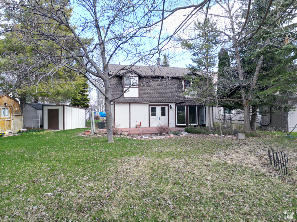Back of property with a lawn, an outdoor structure, roof with shingles, and a shed