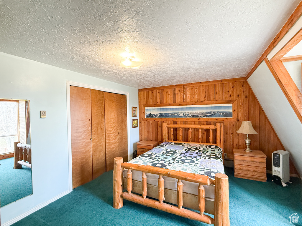 Bedroom featuring carpet floors, wood walls, a textured ceiling, and a closet