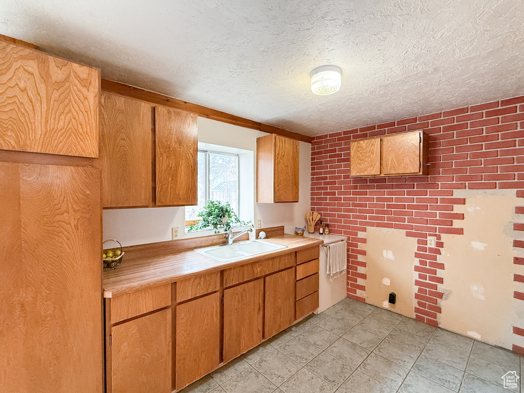 Kitchen with light countertops, a sink, a textured ceiling, and light tile patterned floors