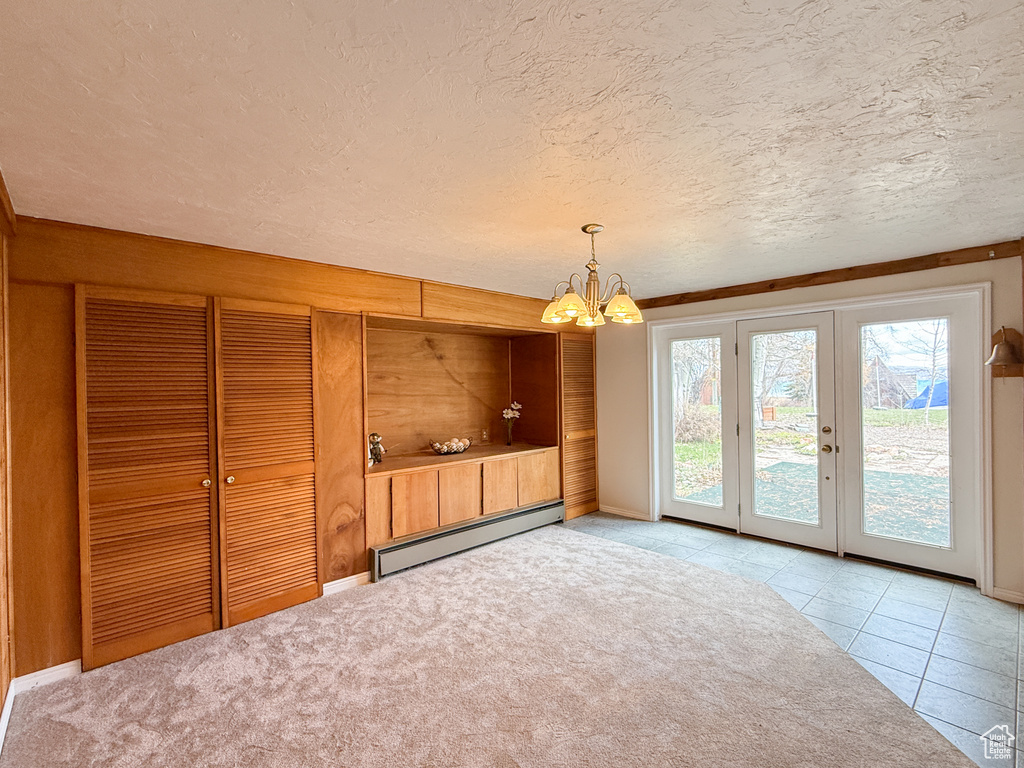 Unfurnished dining area featuring a chandelier, a textured ceiling, baseboard heating, and french doors