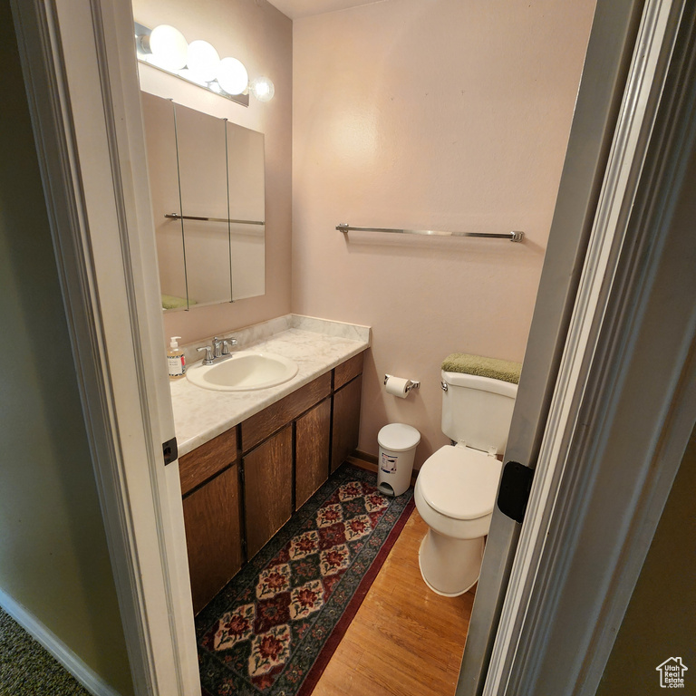 Half bathroom with vanity, baseboards, wood finished floors, and toilet