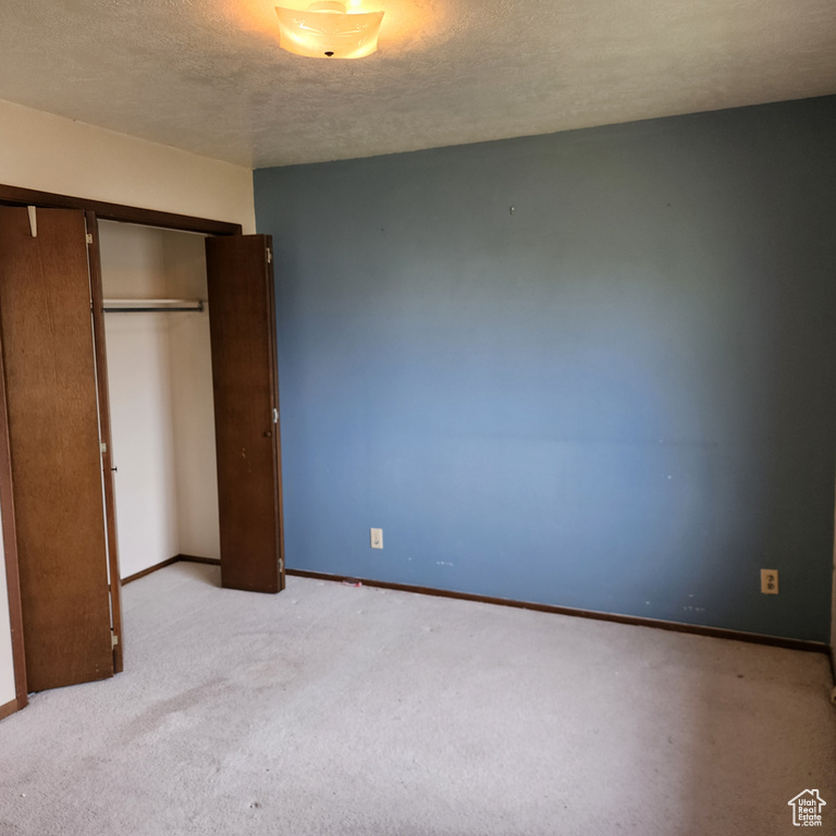 Unfurnished bedroom with a textured ceiling, baseboards, light colored carpet, and a closet
