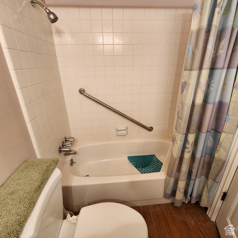 Bathroom featuring shower / bath combo with shower curtain, wood finished floors, and toilet