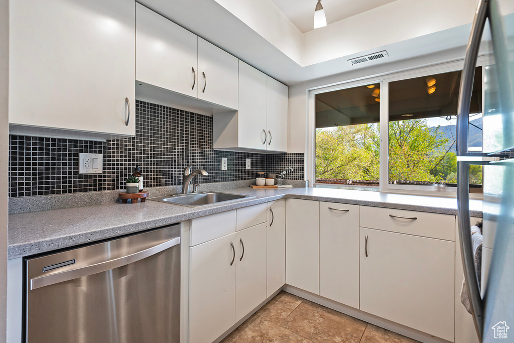 Kitchen featuring stainless steel dishwasher, visible vents, white cabinetry, tasteful backsplash, and a sink