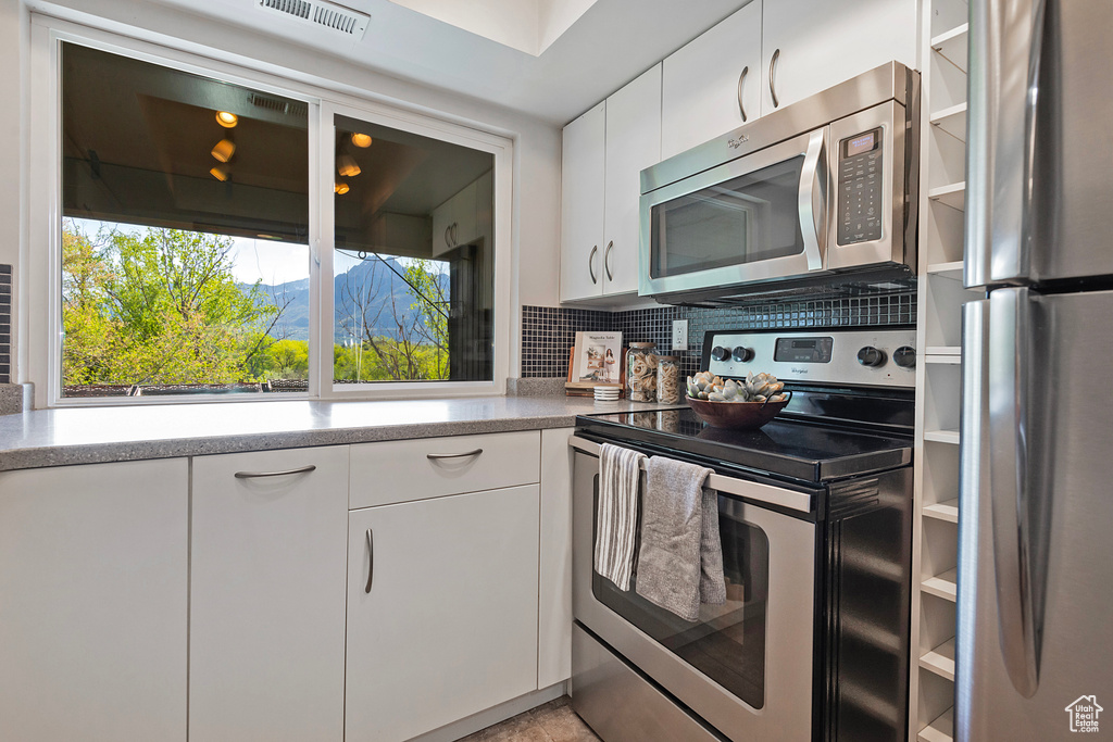 Kitchen with white cabinets, light countertops, stainless steel appliances, backsplash, and visible vents