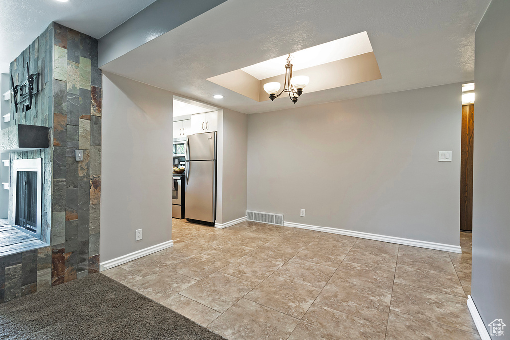 Unfurnished room with visible vents, baseboards, a tray ceiling, a chandelier, and a tiled fireplace